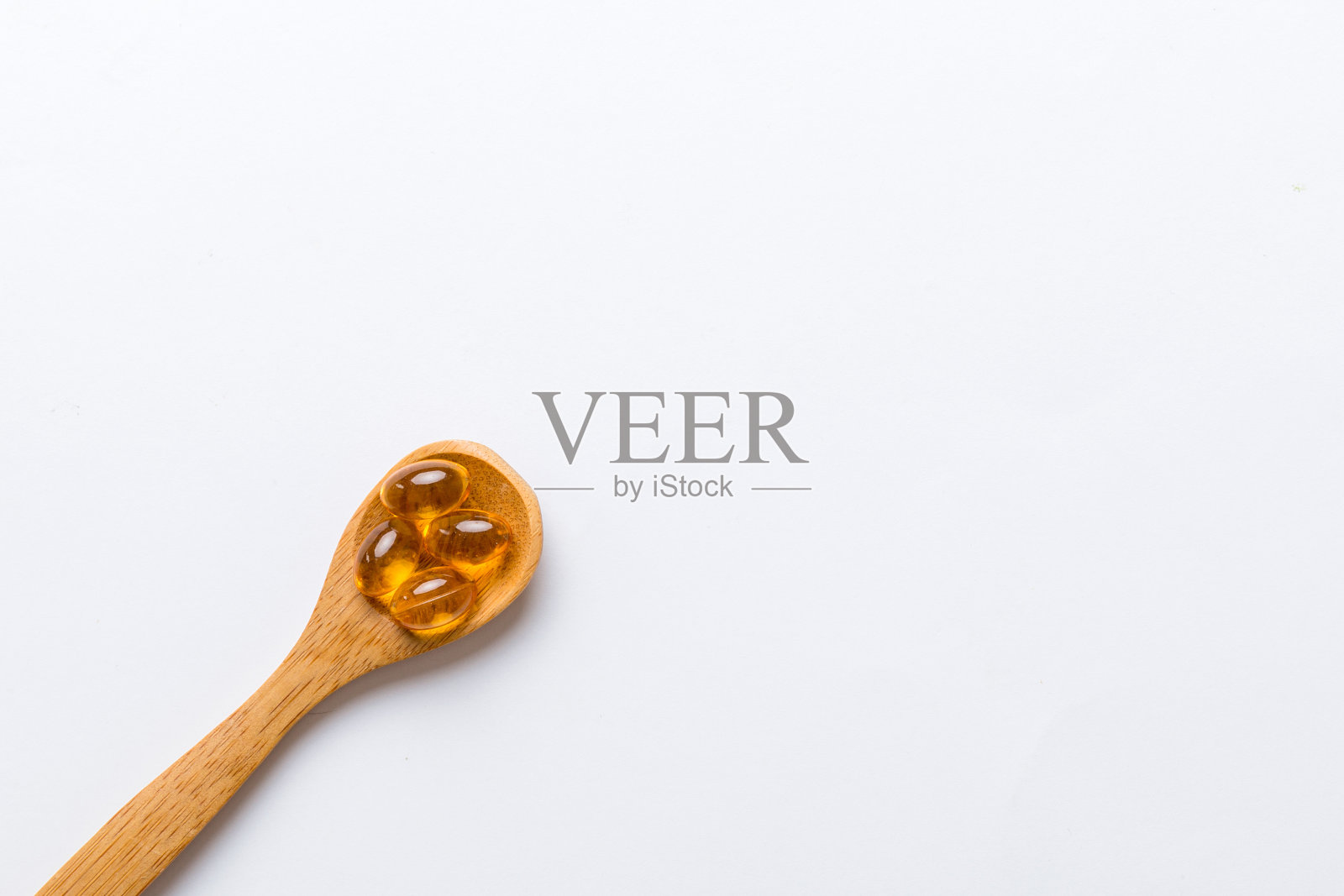 维生素欧米茄胶囊装在一个有色背景的勺子里。药片是健康的一餐。勺子上的红色软凝胶维生素补充胶囊照片摄影图片