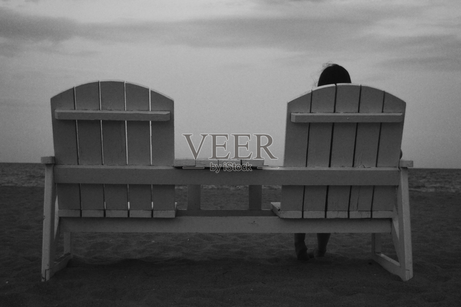 一个女孩正坐在沙滩上的木凳上，面朝大海，黑白照片照片摄影图片