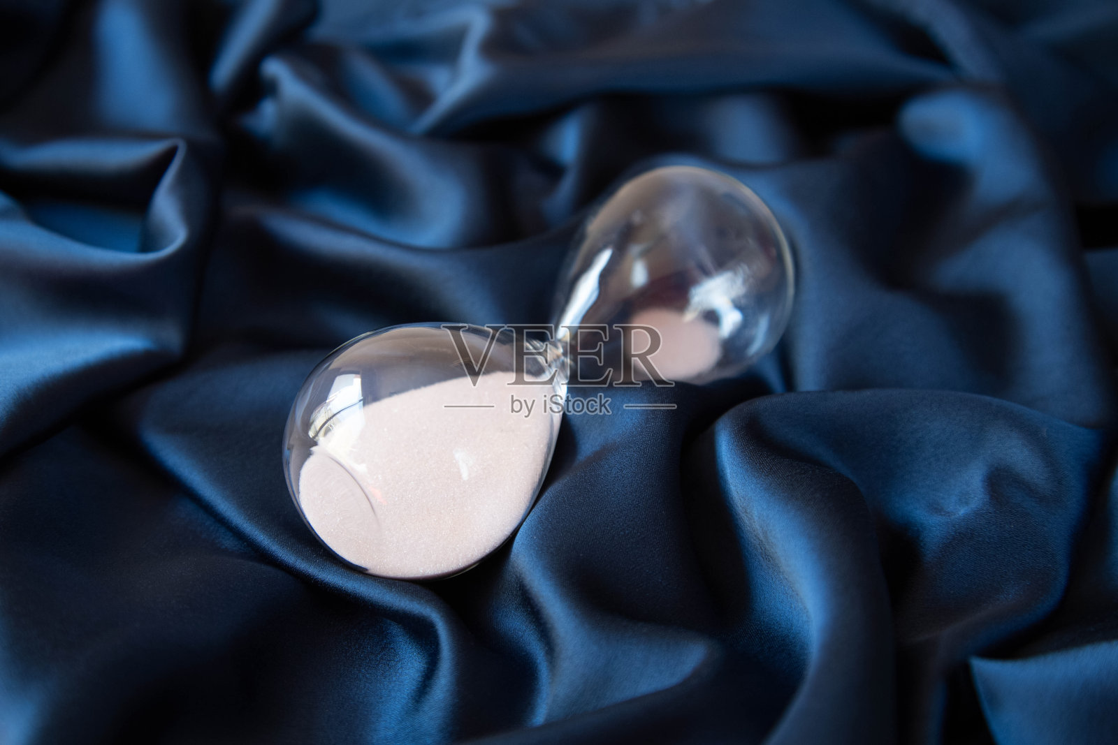 一个沙漏与粉红色的沙子是深蓝色缎面材料。停止时间的概念。照片摄影图片