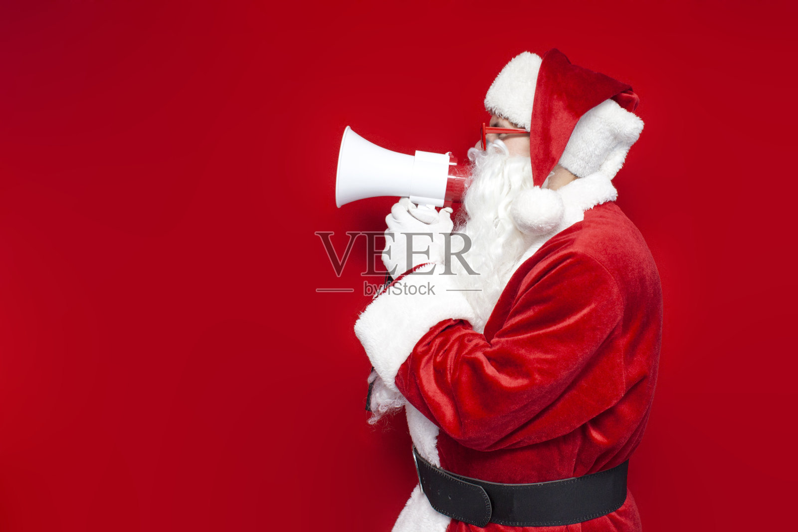 戴着红色眼镜的圣诞老人在彩色背景上对着扩音器宣布信息照片摄影图片