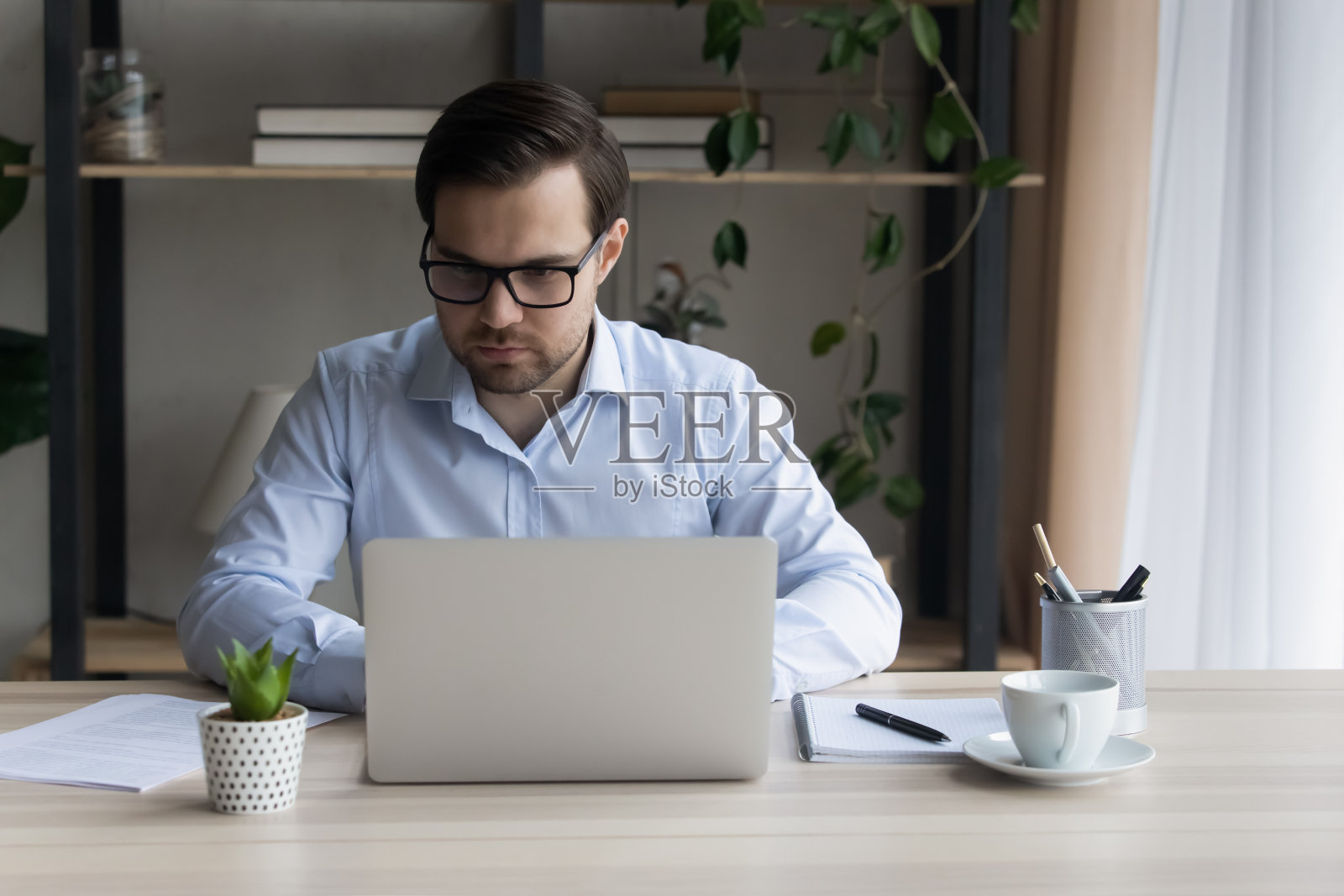 年轻严肃的商人坐在桌前用笔记本电脑工作照片摄影图片