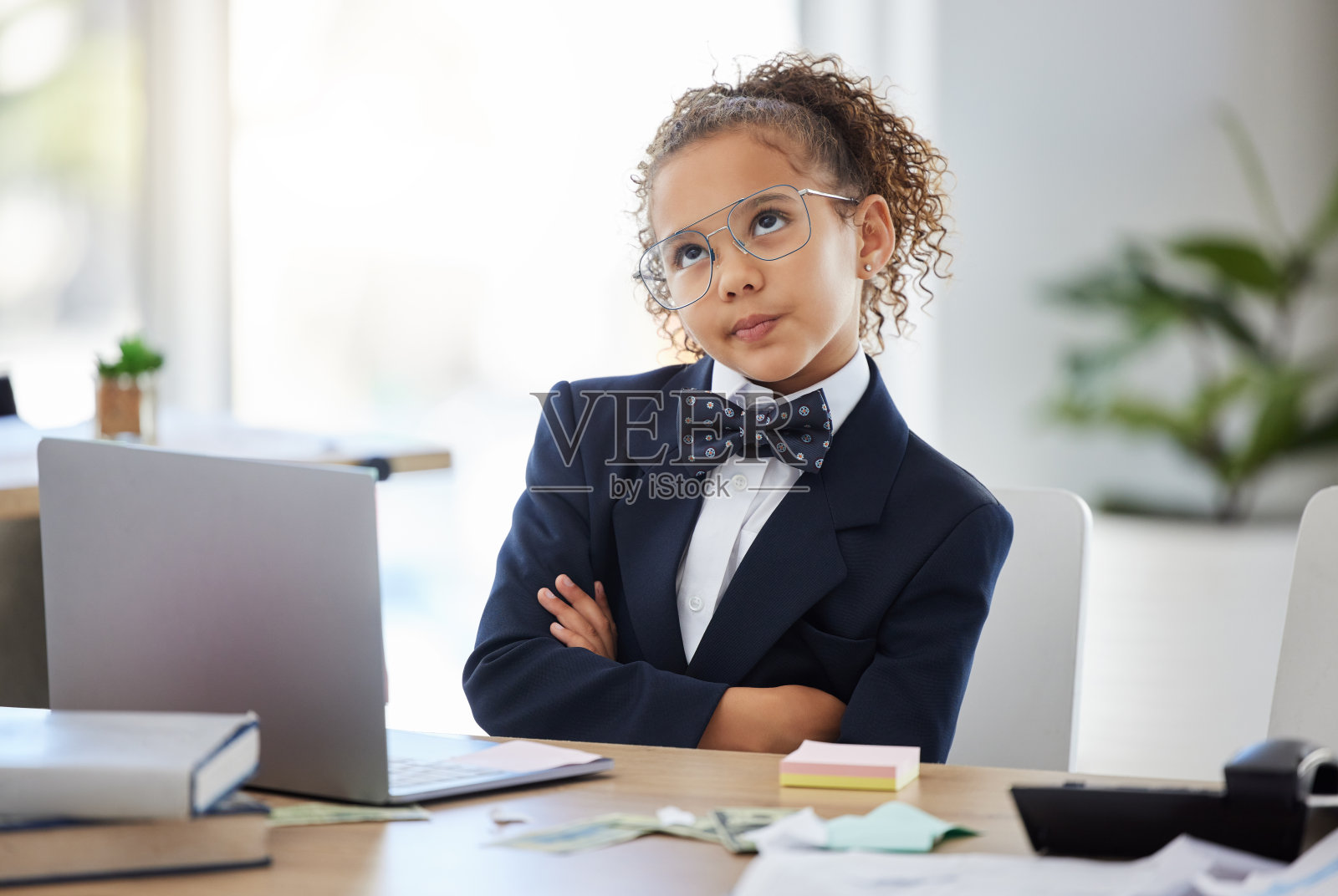 这张照片拍摄的是一个可爱的小女孩，她打扮成一个商人，双臂交叉坐在那里，看起来沉思照片摄影图片