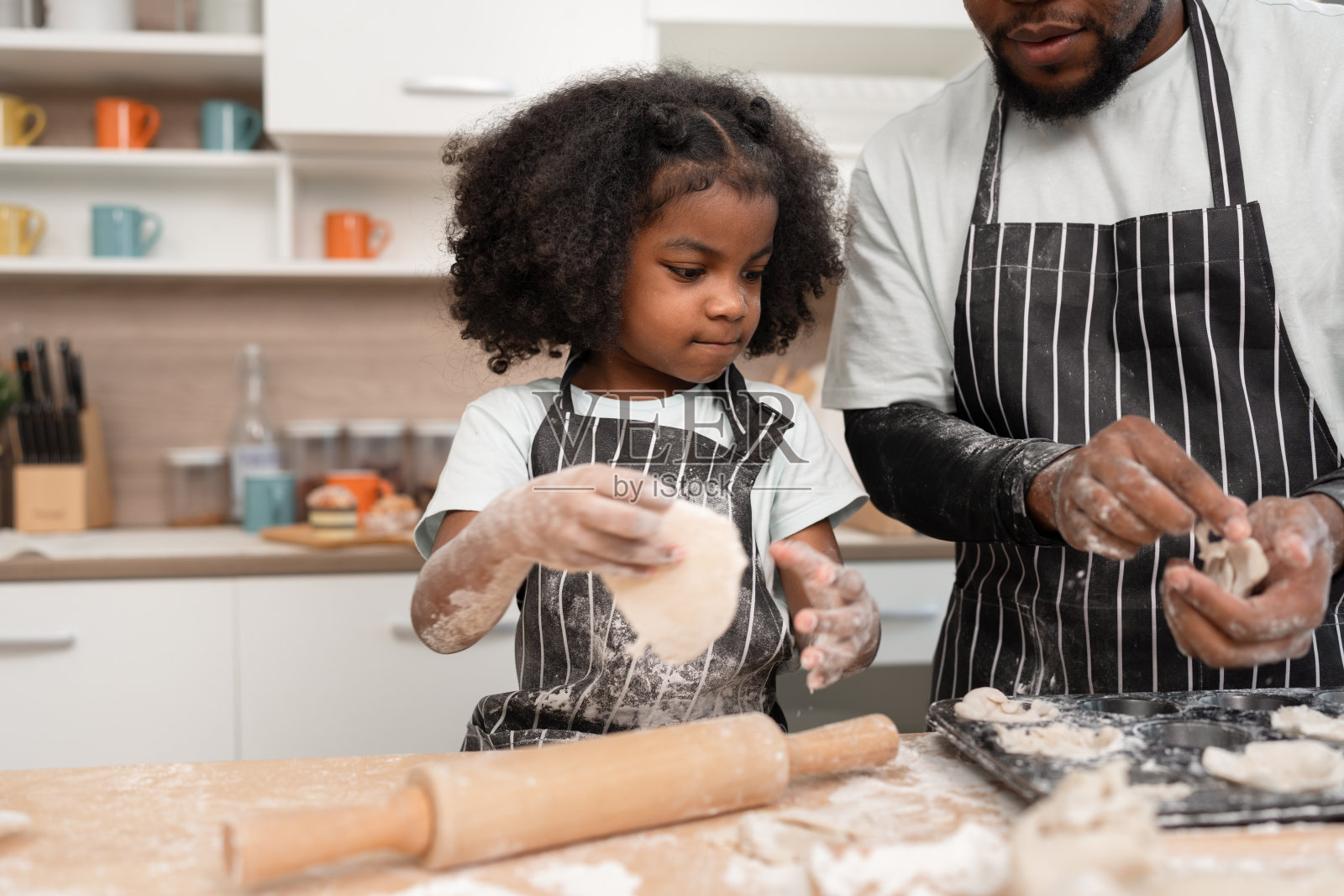 快乐的非裔美国女孩和父亲在家里的厨房里做饭或烤面包照片摄影图片