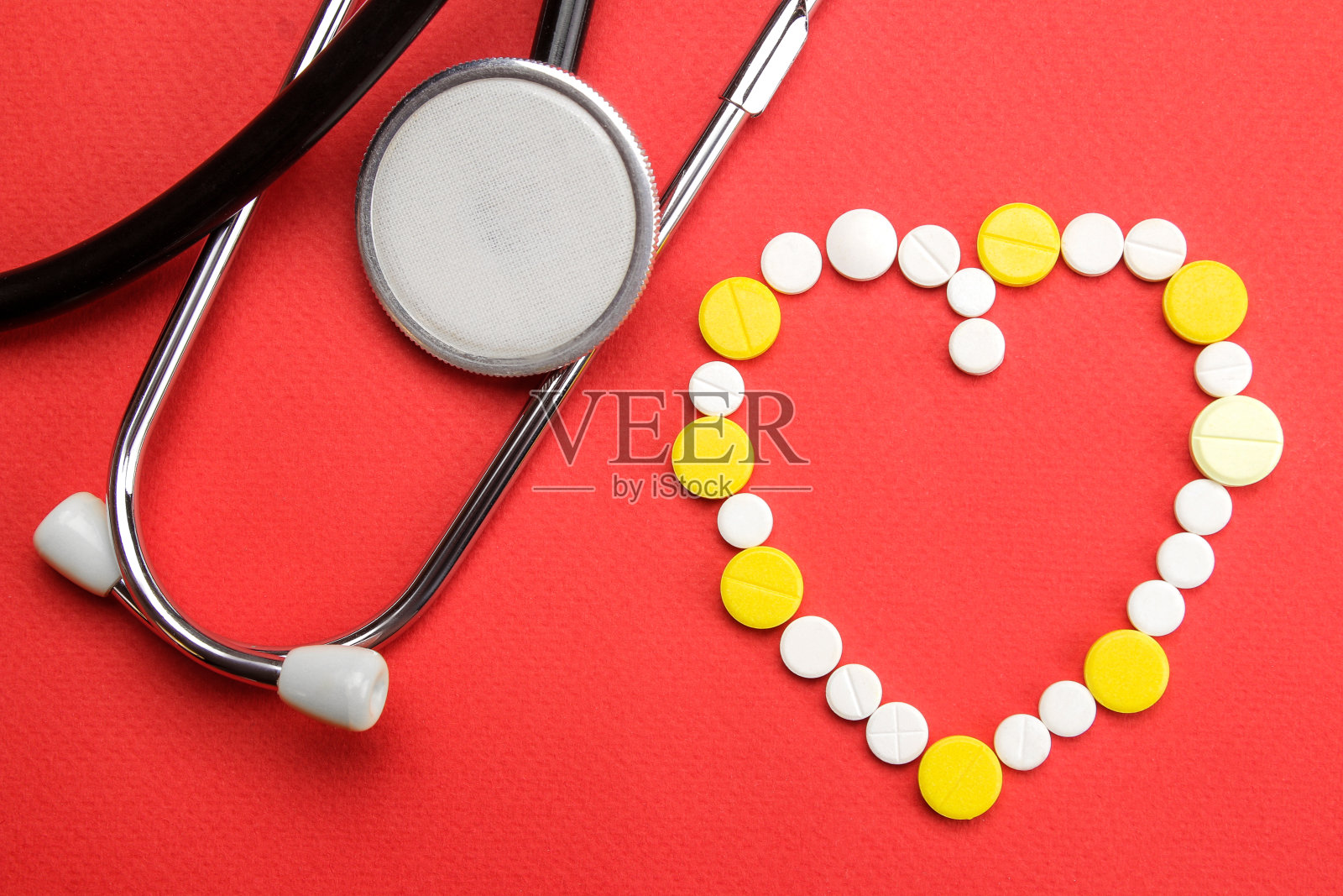 心脏由药丸和红色背景上的听诊器组成。从上面看。心脏病学和心脏健康。照片摄影图片