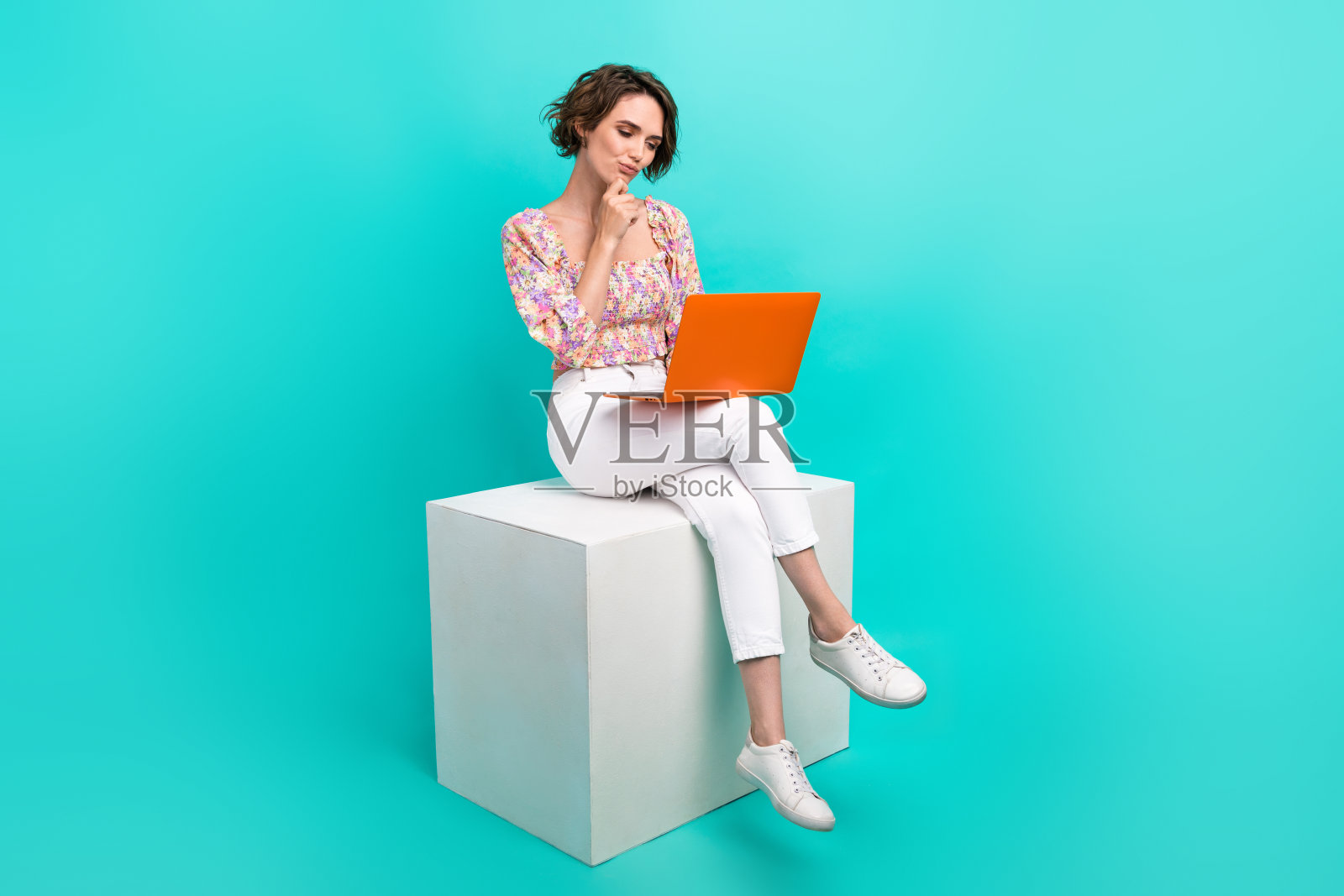 心地善良的人的全身照片坐在讲台上，手摸下巴头脑风暴使用上网本孤立的青色背景照片摄影图片