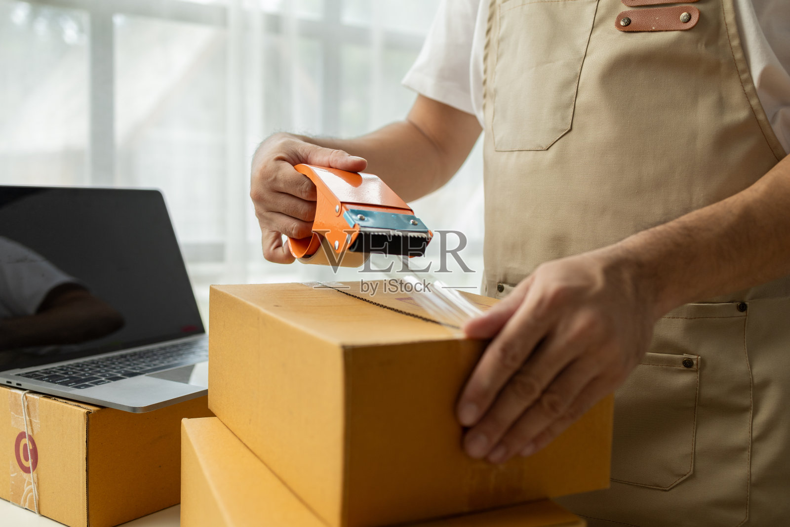 一家网店的男老板根据网上销售网站的订单，将商品包装成包裹盒，通过私人快递服务将商品包装到地址。产品包装理念。照片摄影图片