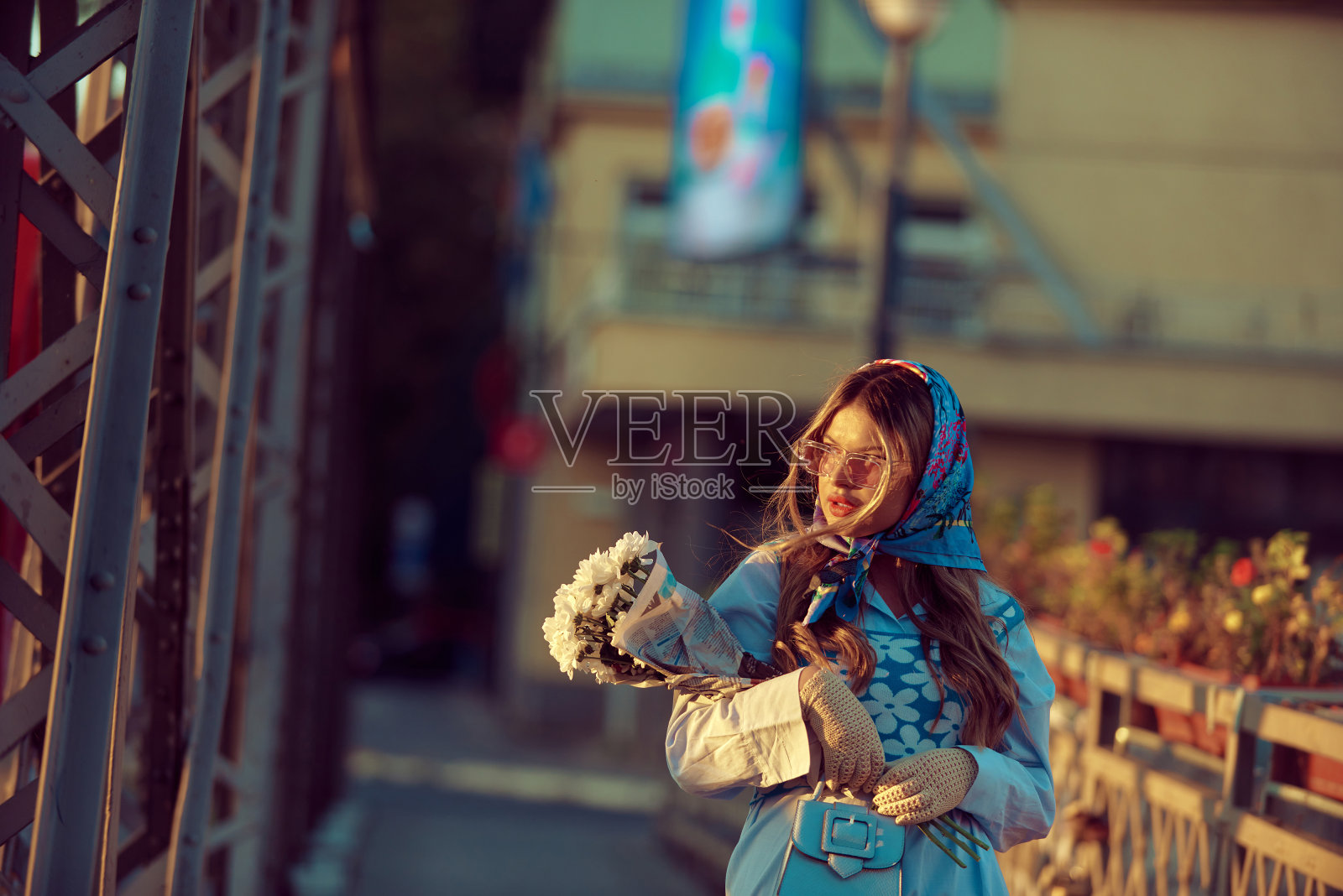 魅力的女人穿着精致的蓝色传统服装，背着蓝色的手提包和一束花，优雅地漫步在日落时分的城市，创造了一个迷人的场景，优雅，文化丰富，宁静的氛围照片摄影图片