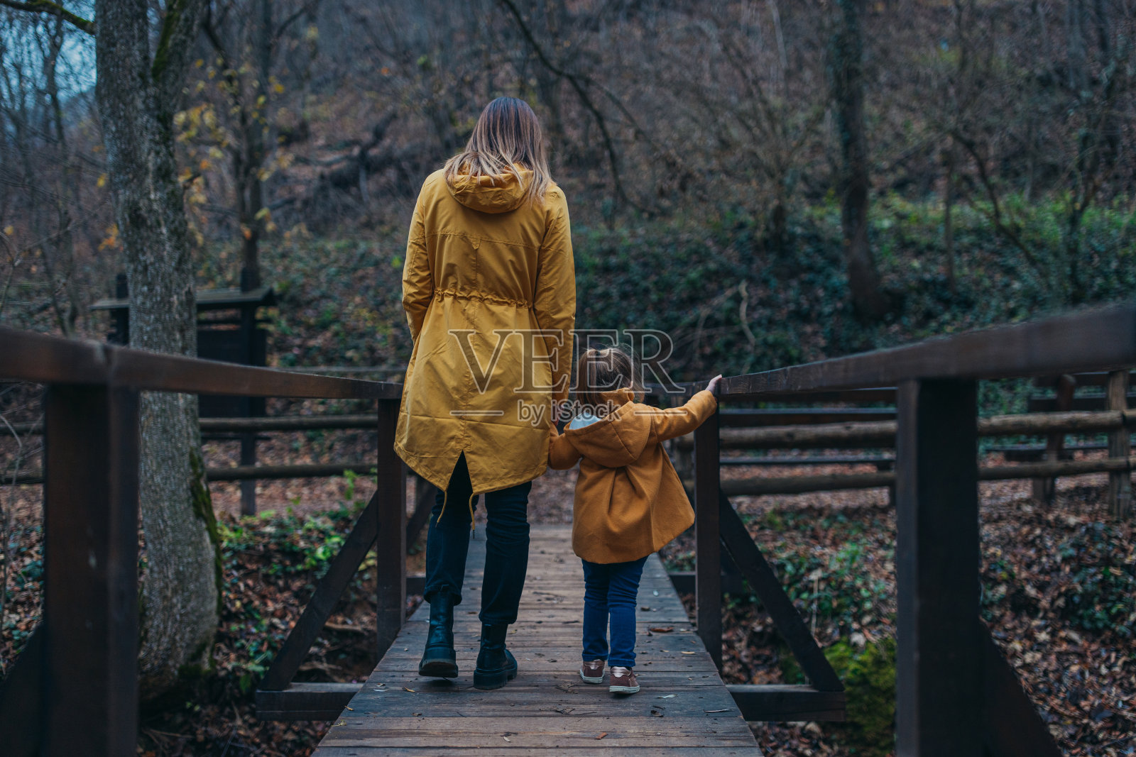 一个小女孩把手放在桥上，和妈妈一起走过桥照片摄影图片