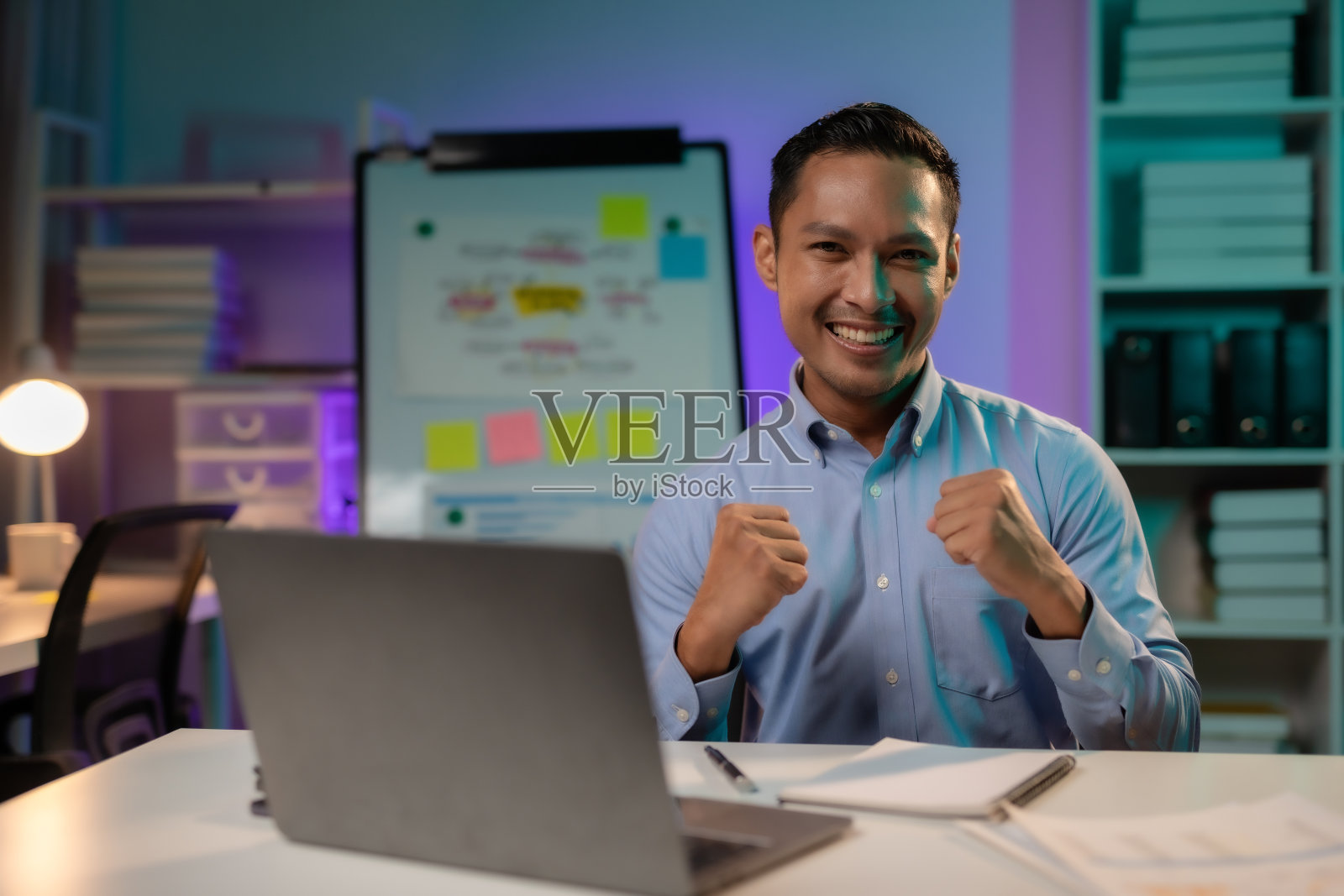 成就解锁。亚洲商人加班成功后高举双臂庆祝胜利。照片摄影图片