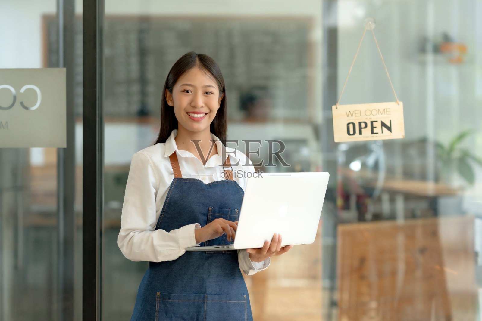 漂亮的亚洲企业主拿着笔记本电脑站在门口，在网上接受顾客的订单。照片摄影图片