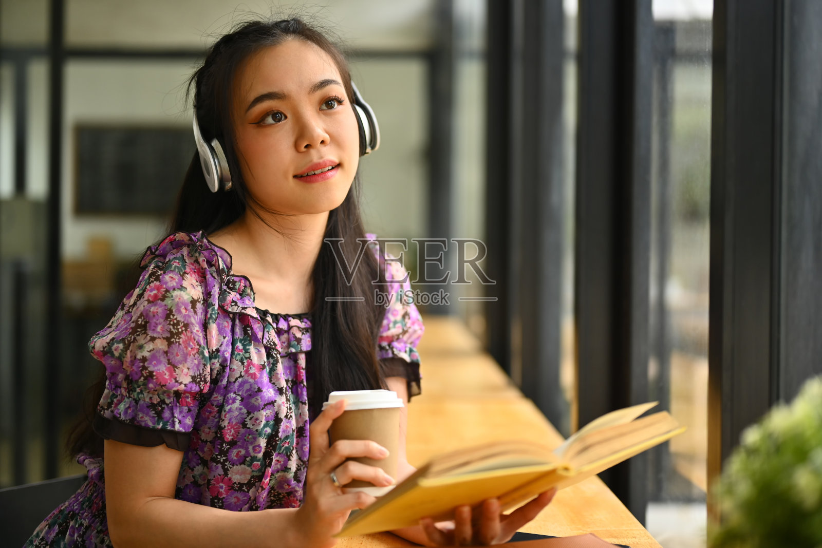 梦幻的年轻女大学生戴着耳机拿着纸杯，看向别处照片摄影图片