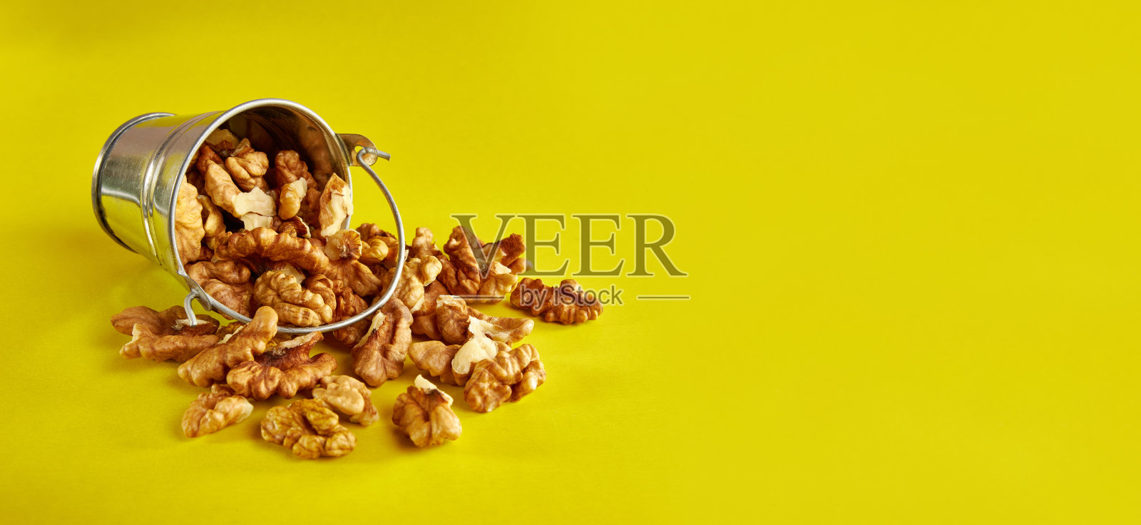 一个小金属桶，里面装满了黄色背景的核桃。健康饮食的概念。照片摄影图片