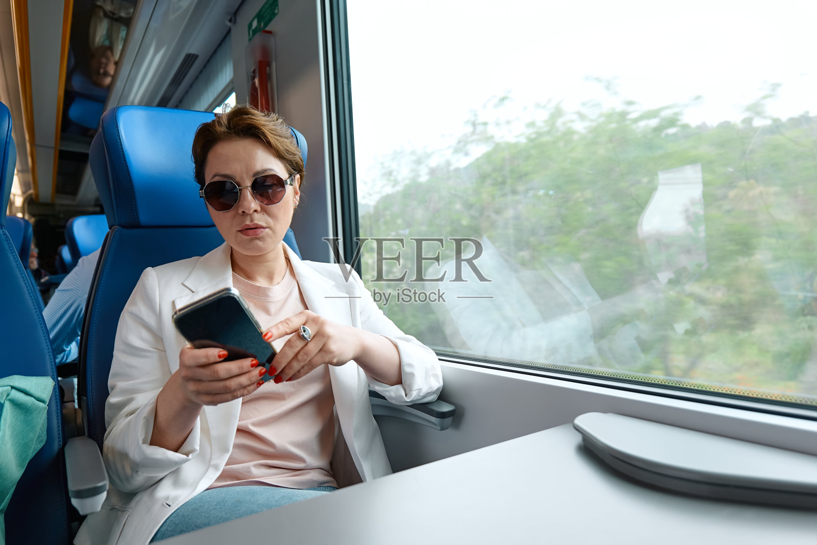 严肃的女商人自由博客在火车上使用手机。乘火车旅行的美女游客坐在靠窗的地方，用智能手机工作或玩社交媒体。照片摄影图片