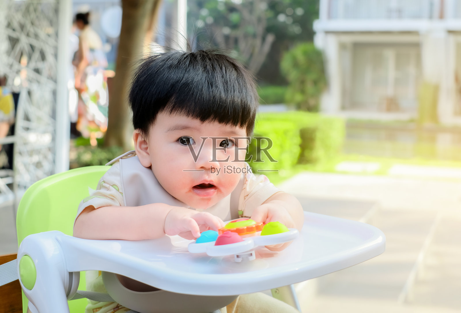亚洲宝宝用凌乱的嘴坐在户外的宝宝喂食椅上，宝宝边吃边玩的概念照片摄影图片