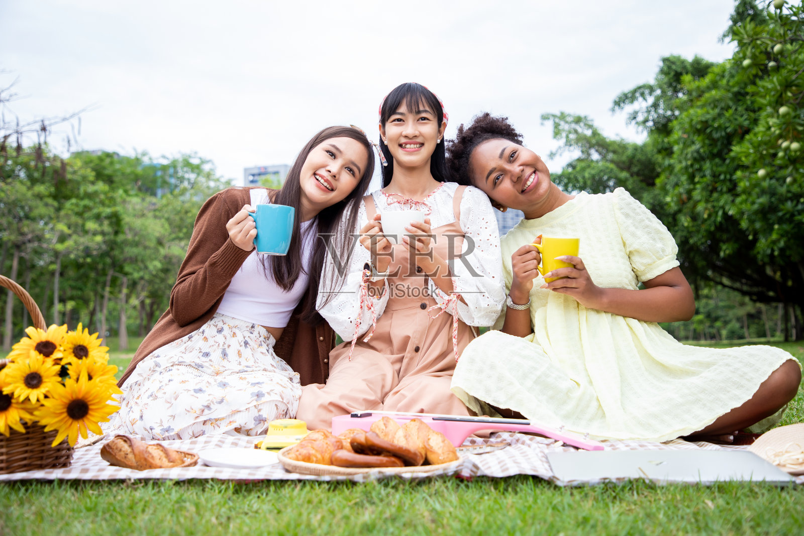 在公园野餐时，年轻女子喝着棕色托盘上的法棍面包和椒盐卷饼饮料。照片摄影图片