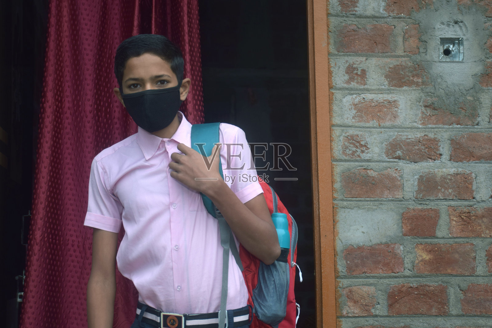 冠状病毒大流行中，十几岁的男孩穿着校服，戴着口罩，背着书包上学照片摄影图片