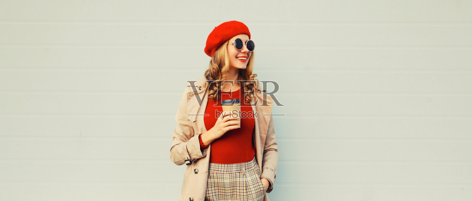 秋季风格的服装，时尚快乐微笑的年轻女子模特与一杯咖啡戴红色法国贝雷帽，夹克和圆形太阳镜在灰色背景照片摄影图片
