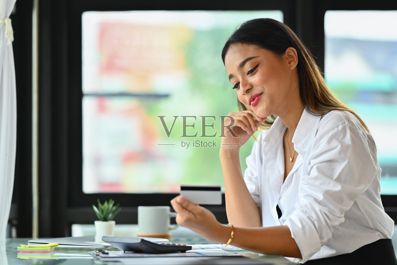 漂亮的女工拿着信用卡，面带微笑。网上购物，电子商务，网上银行的概念照片摄影图片