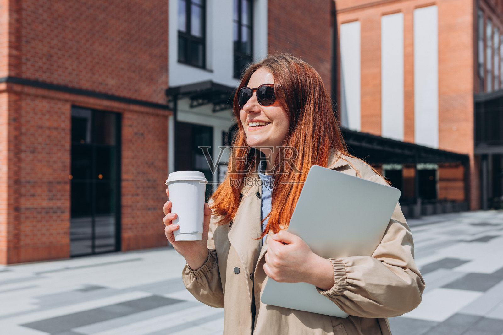 白种红发女商人，穿着时尚的办公室服装，拿着笔记本电脑和生态茶在外面摆姿势。模型，女人用笔记本电脑和拿着生物白色的咖啡杯照片摄影图片