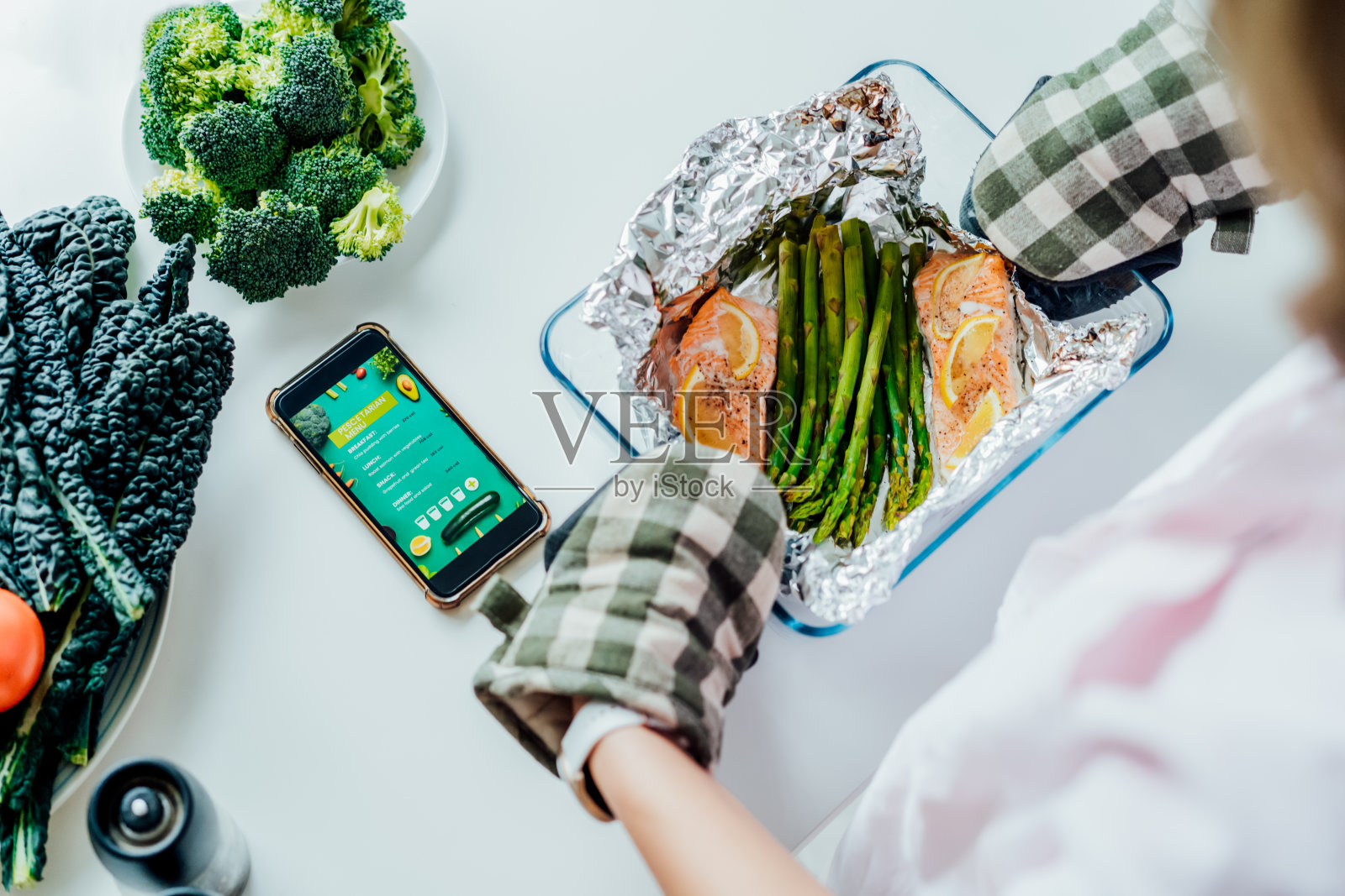 鱼素饮食食谱。俯视图妇女保持形式与烤鲑鱼和芦笋。桌上放着移动鱼素菜单的手机。健康饮食，减肥理念。照片摄影图片