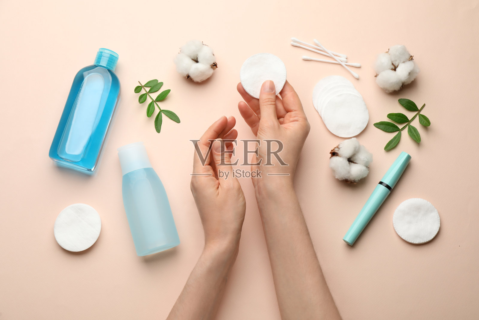 在米色的背景下，女人拿着化妆棉垫接近卸妆产品，俯视图照片摄影图片