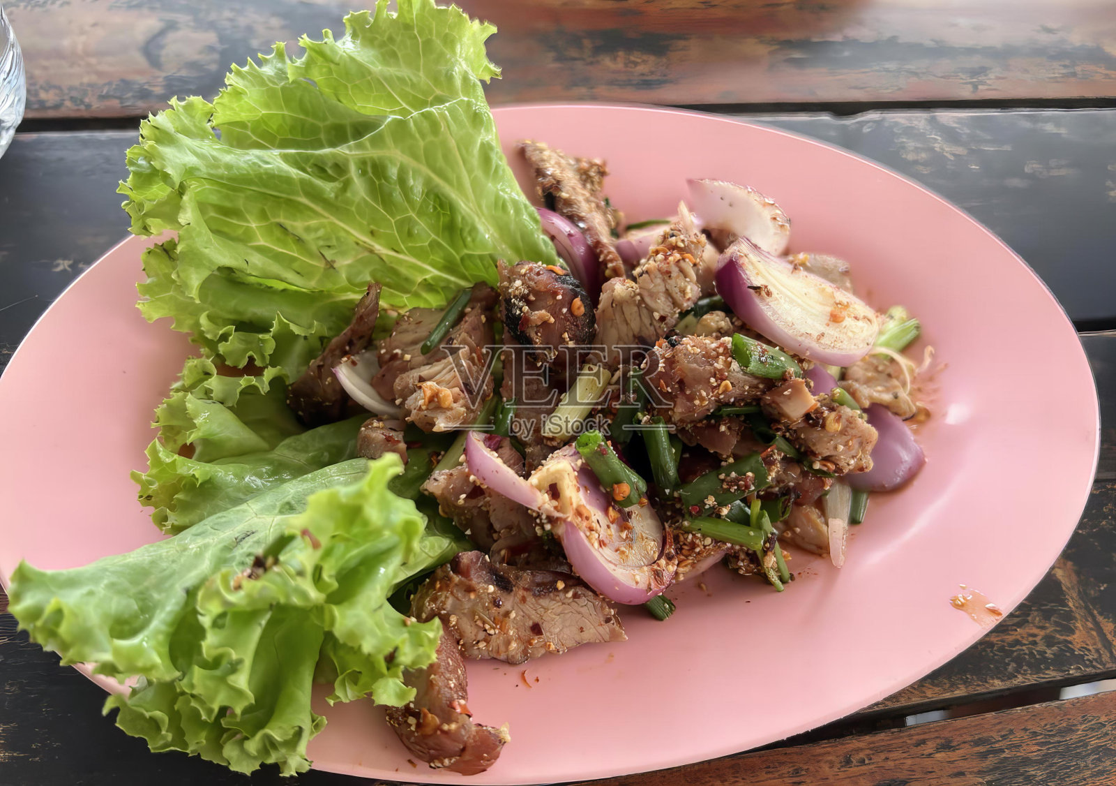 一盘食物的照片，有生菜和肉，肉卷和生菜放在木桌子上的粉红色盘子上。照片摄影图片