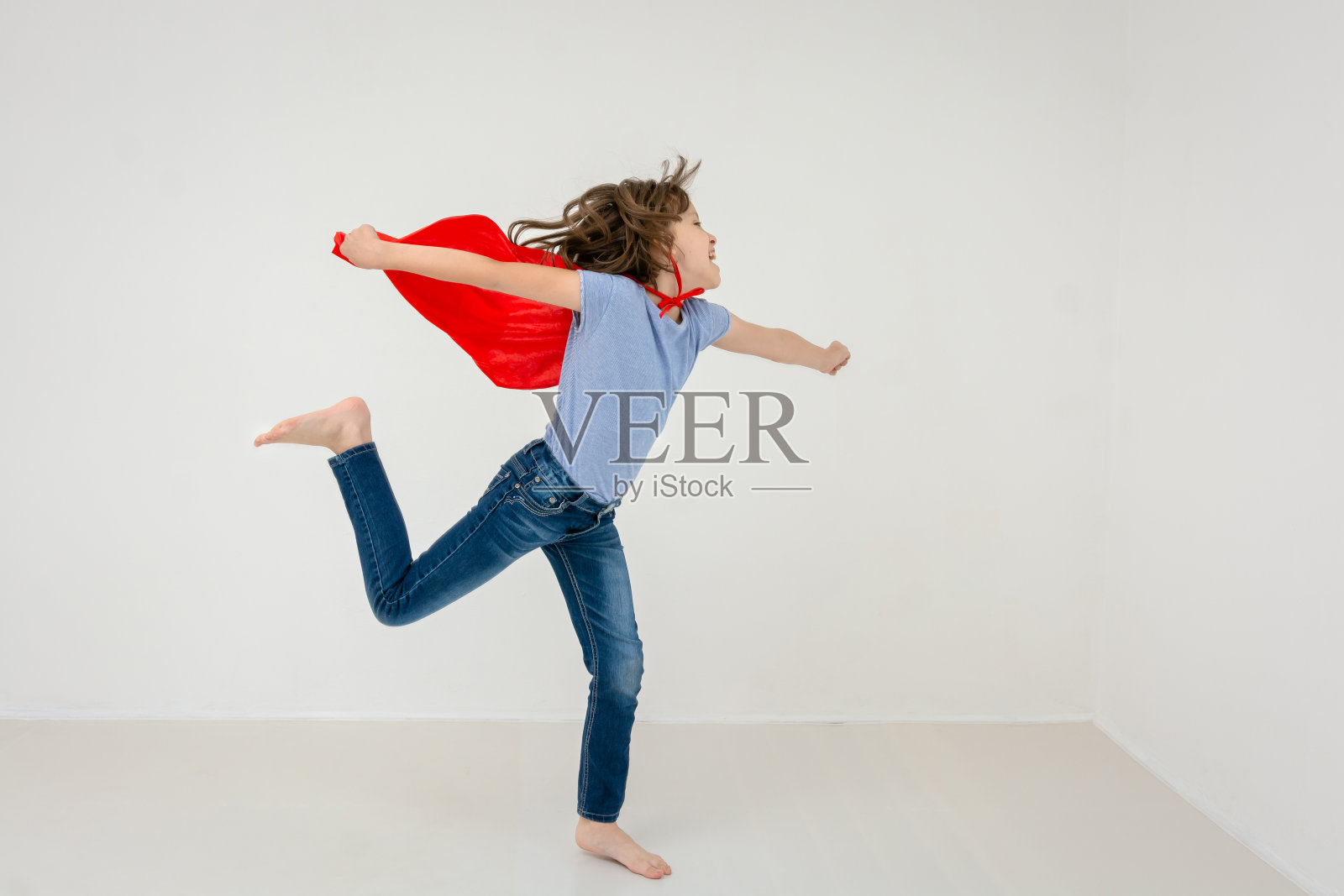 在摄影棚里假装成超级英雄的快乐女孩的肖像照片摄影图片