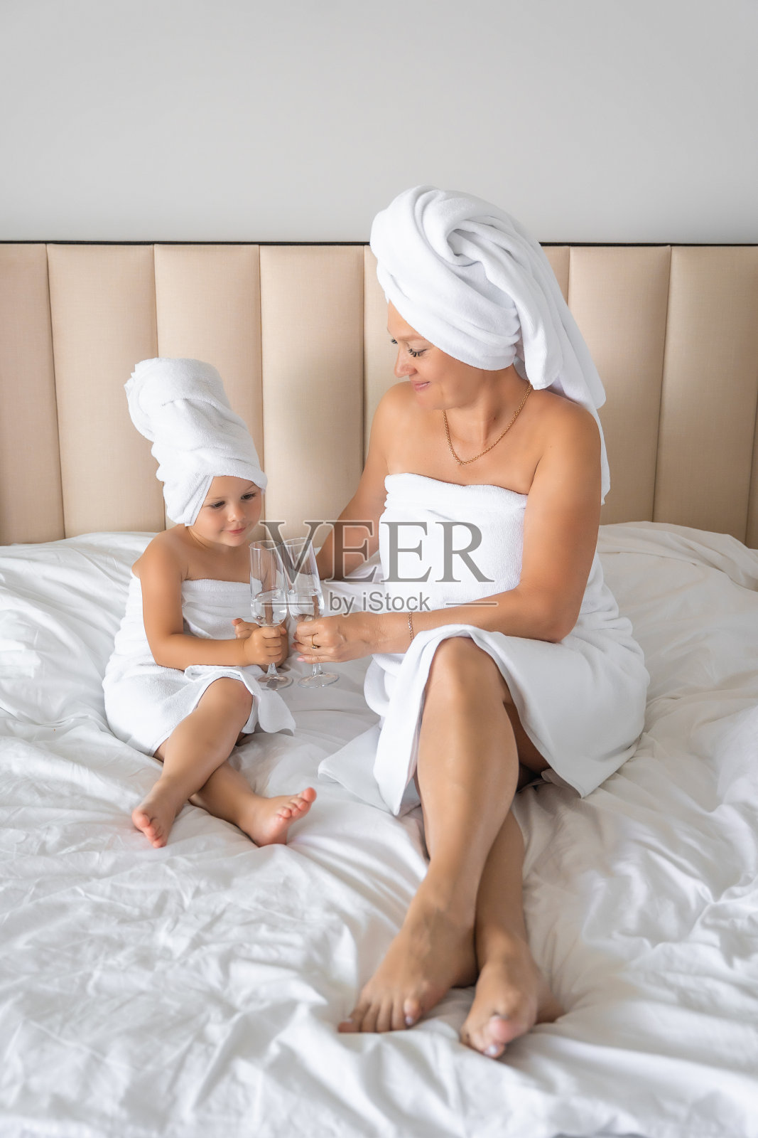 幸福的一家人，妈妈和小女儿穿着睡袍，披着毛巾，在家里用玻璃杯喝着水照片摄影图片