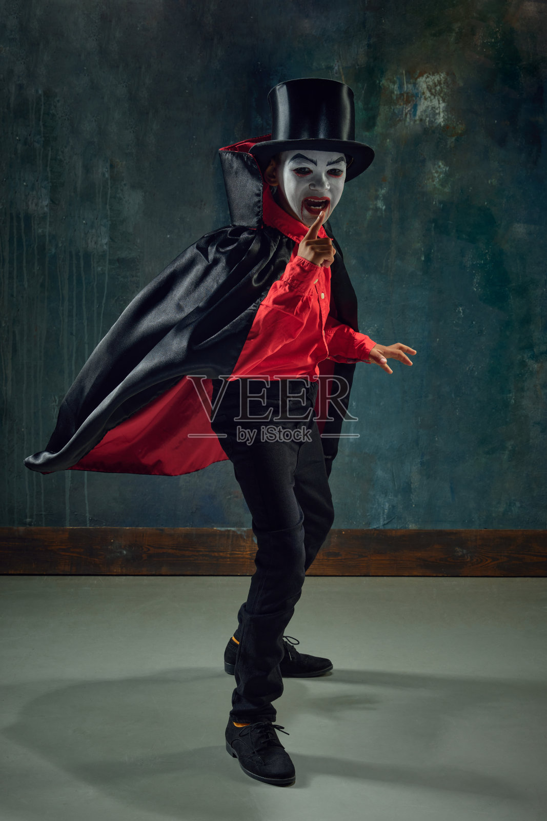 小男孩，在令人毛骨悚然的吸血鬼的形象，穿着服装和化妆在黑暗的复古背景。恐怖照片摄影图片