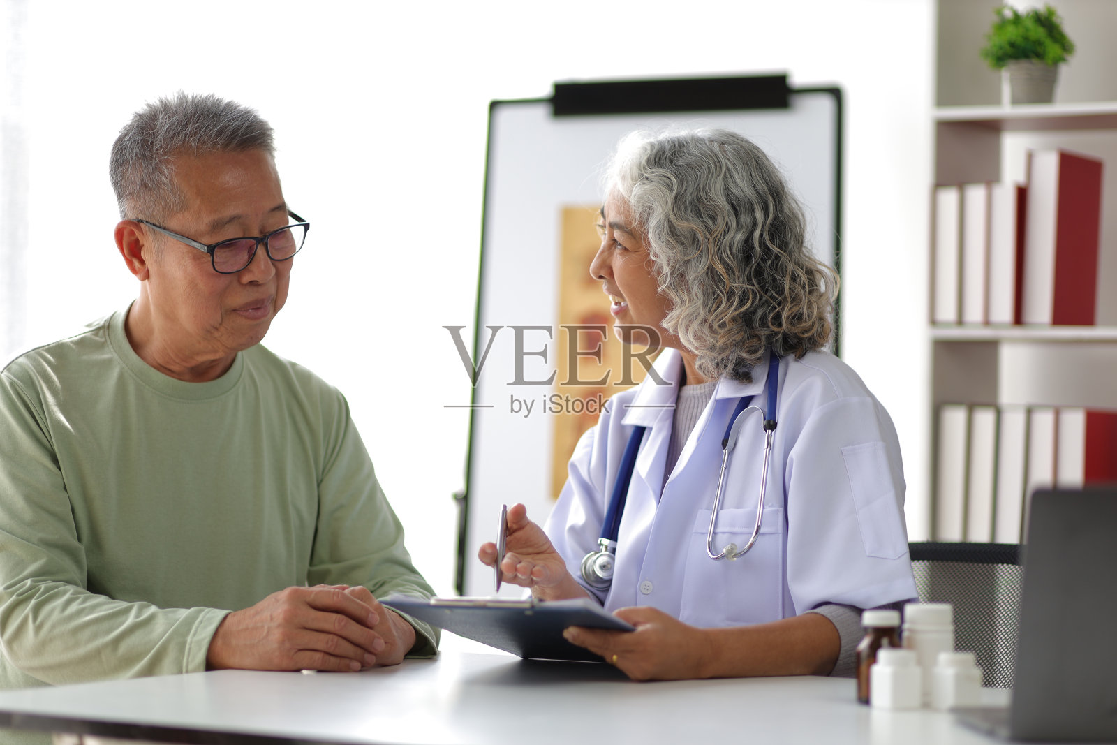 老年保健理念。医生和病人在医务室。一位退休老人坐在医院的检查室里，与医生讨论他的健康状况。照片摄影图片