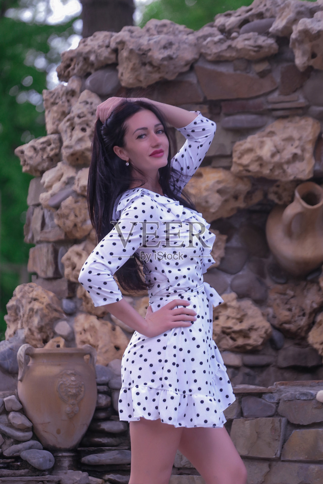 美丽时尚的黑发女子成人摆姿势在装饰石的背景下，白色礼服与波点照片摄影图片