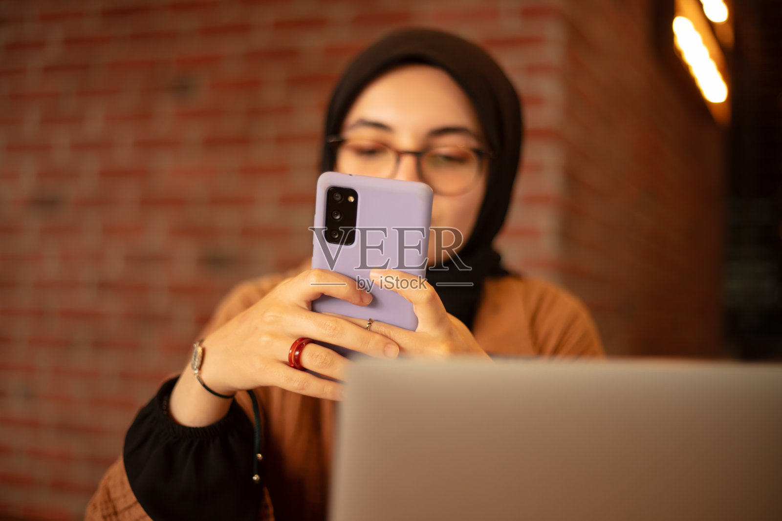 年轻漂亮的头巾妇女正在咖啡馆用手机工作。照片摄影图片