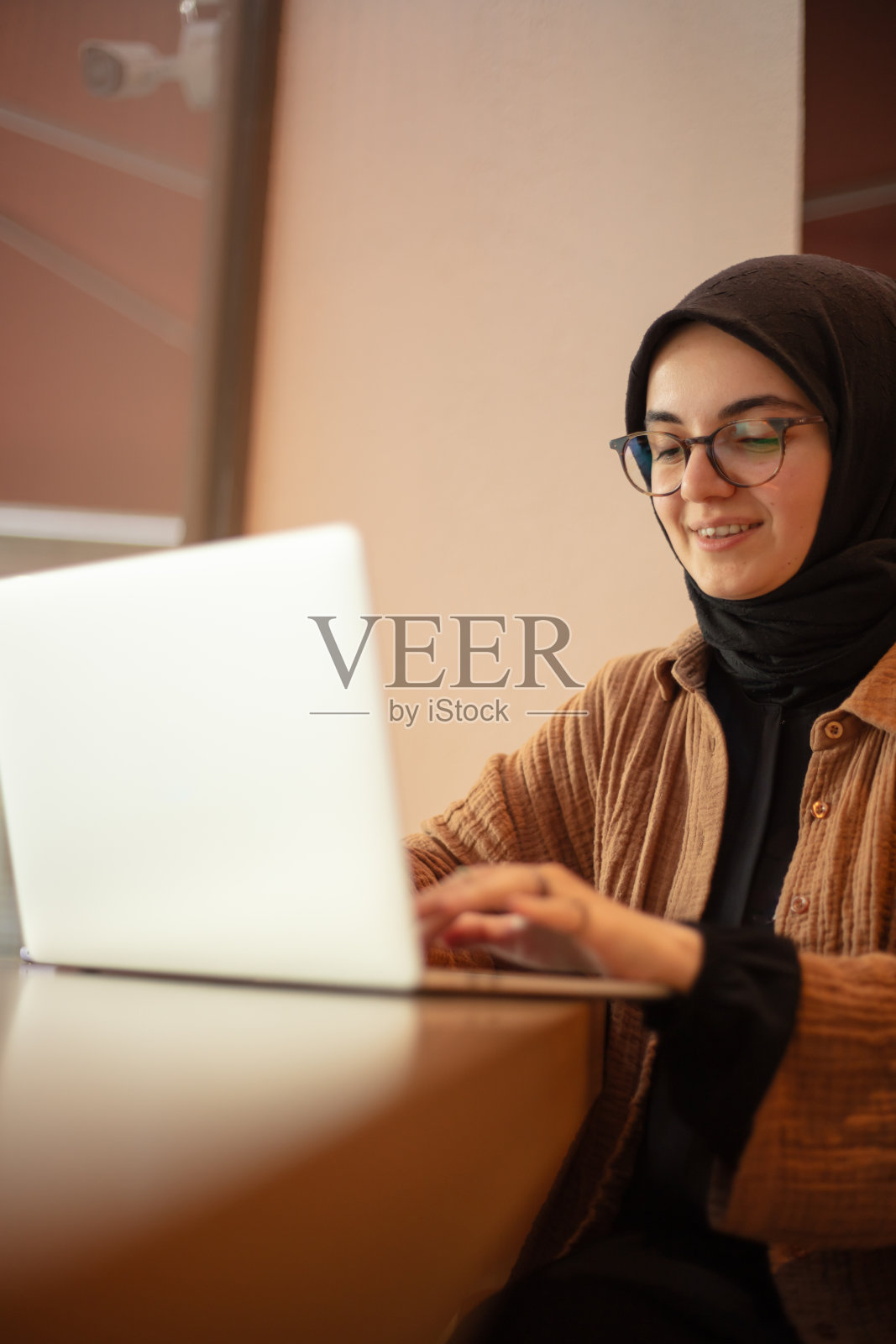 年轻的头巾女士带着美丽的微笑在咖啡店工作。照片摄影图片