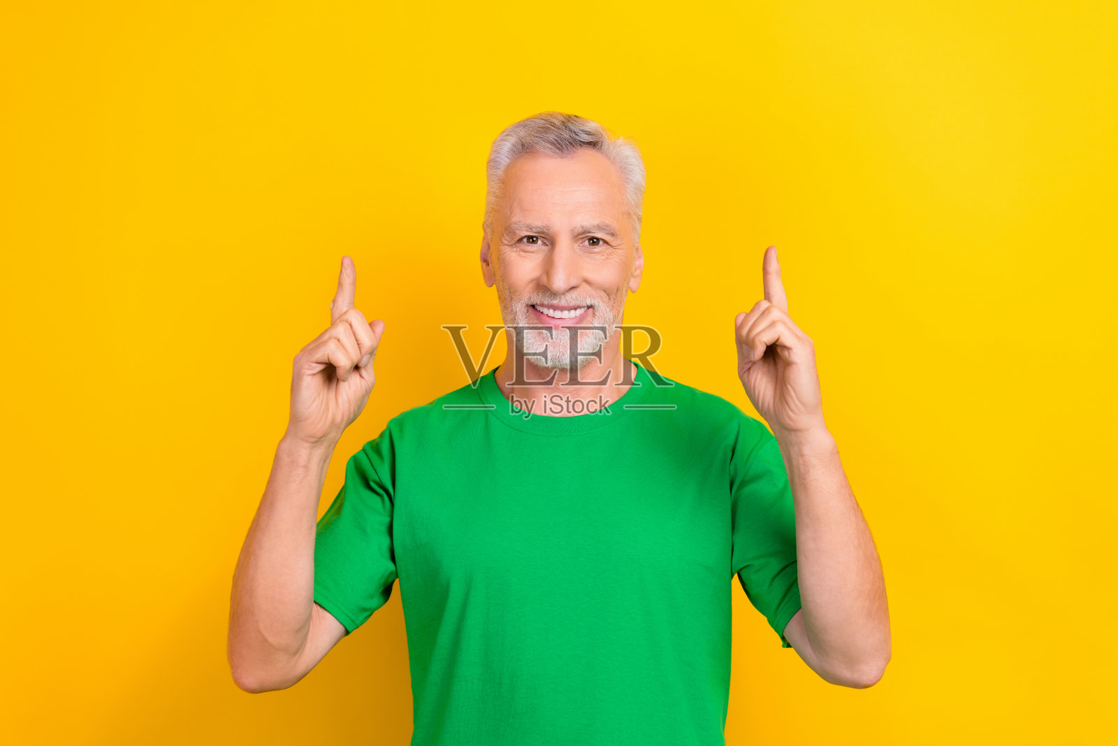 照片中穿着绿色t恤的有趣的积极的家伙用两只手指指着空的空间，孤立的黄色背景照片摄影图片