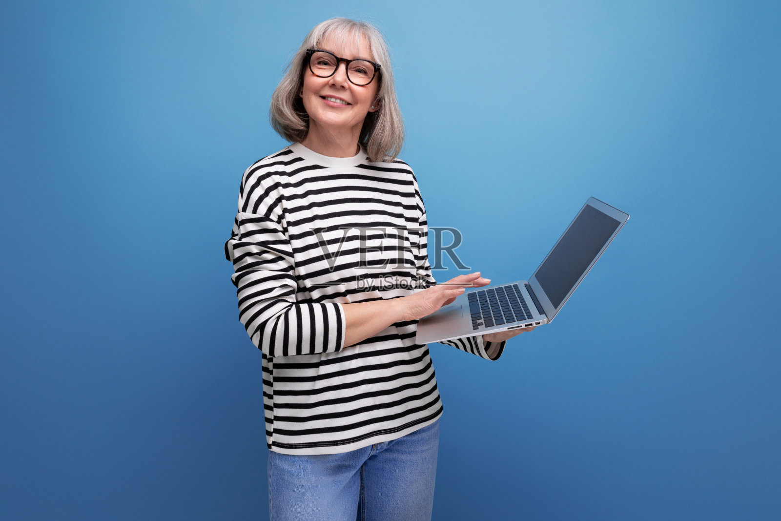 一位成功的60多岁的成熟女性，头发花白，在明亮的工作室背景下用笔记本电脑上网照片摄影图片