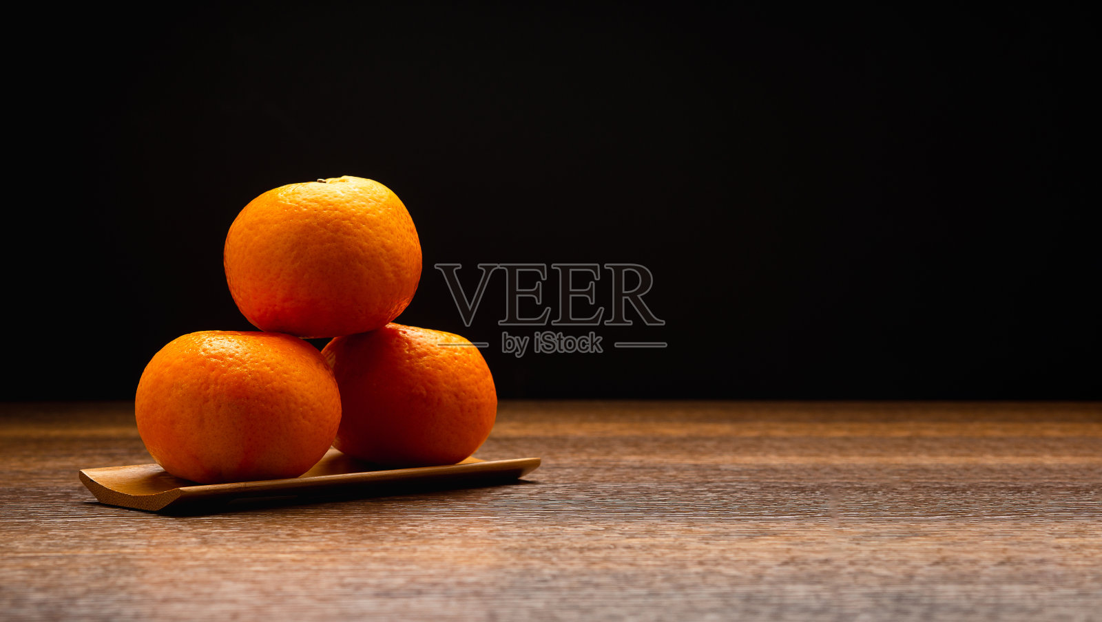 新鲜的橘子放在黑色背景的木桌上的木托盘上照片摄影图片