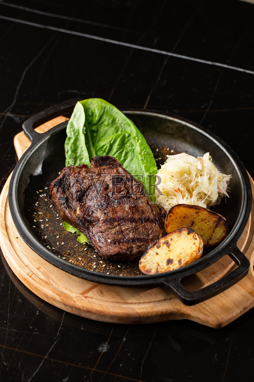 烤牛排、烤土豆、酸菜和红酱在黑色的背景上。美味的食谱。晚餐用煎锅煎猪肉里脊。炒肉汁质地照片摄影图片