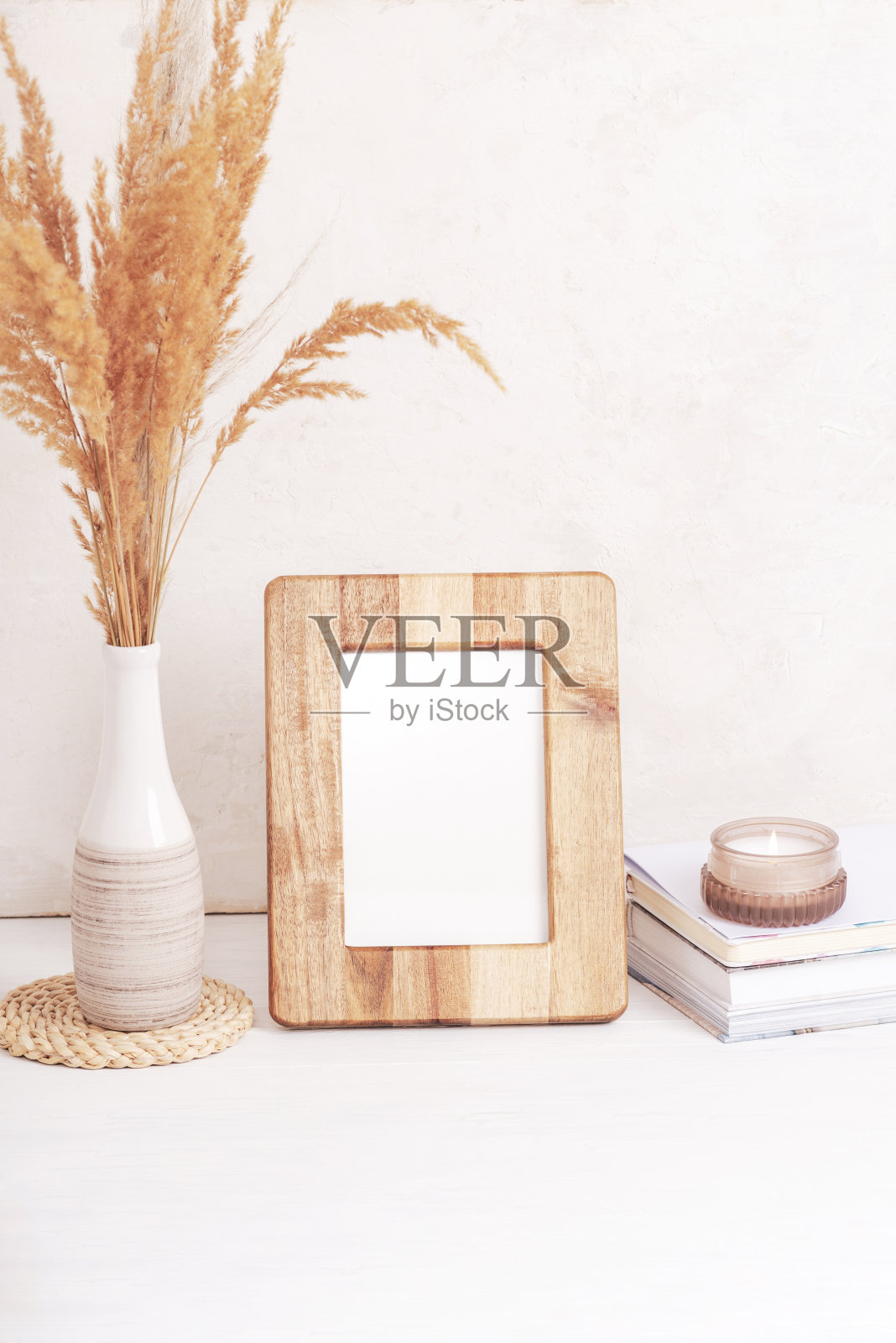 白色桌子上的花瓶里有木制相框、书籍、香薰蜡烛和潘帕斯草的模型。本空间照片摄影图片