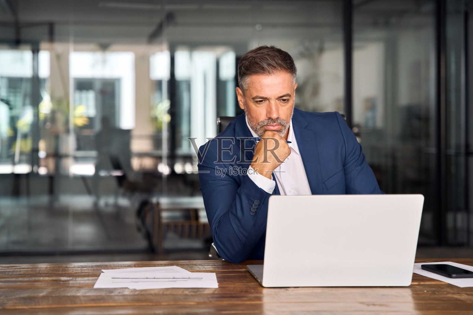 成熟的印度或拉丁商人首席执行官使用电脑，打字，在现代办公室工作，做在线数据市场分析，思考规划技术战略，看着笔记本电脑复印空间。照片摄影图片