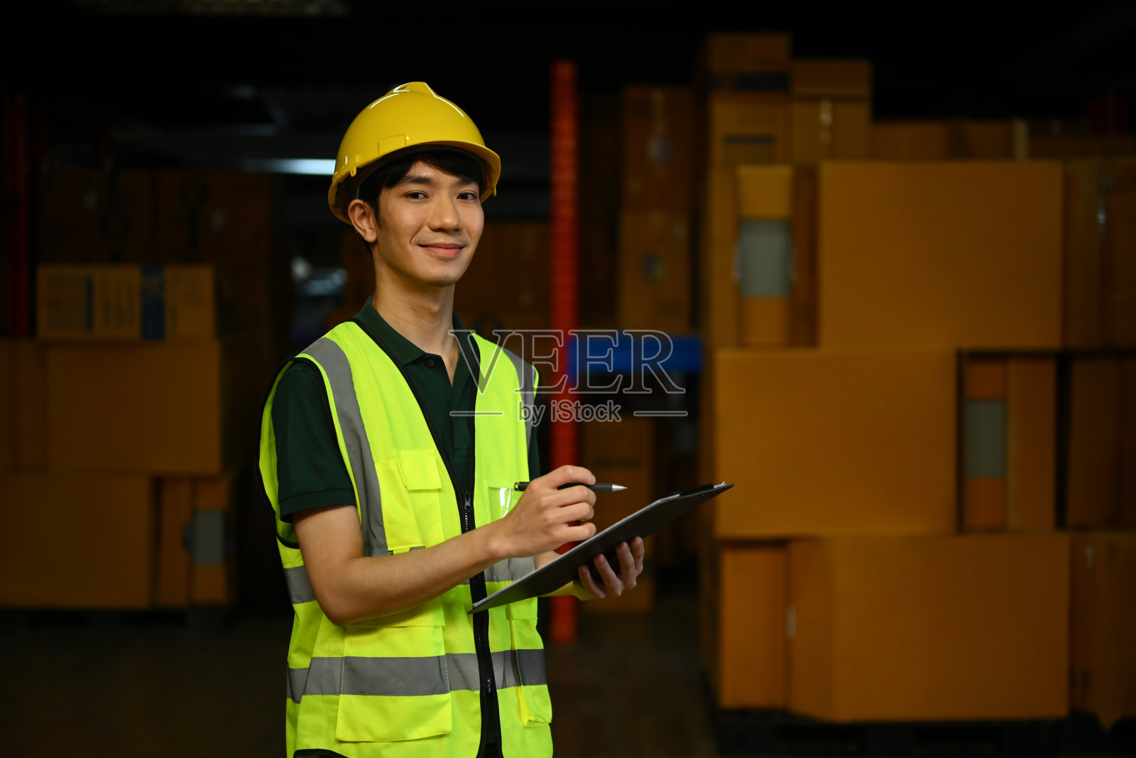 男工人戴安全帽，穿背心，在大型仓库检查货架上储存产品的数量照片摄影图片