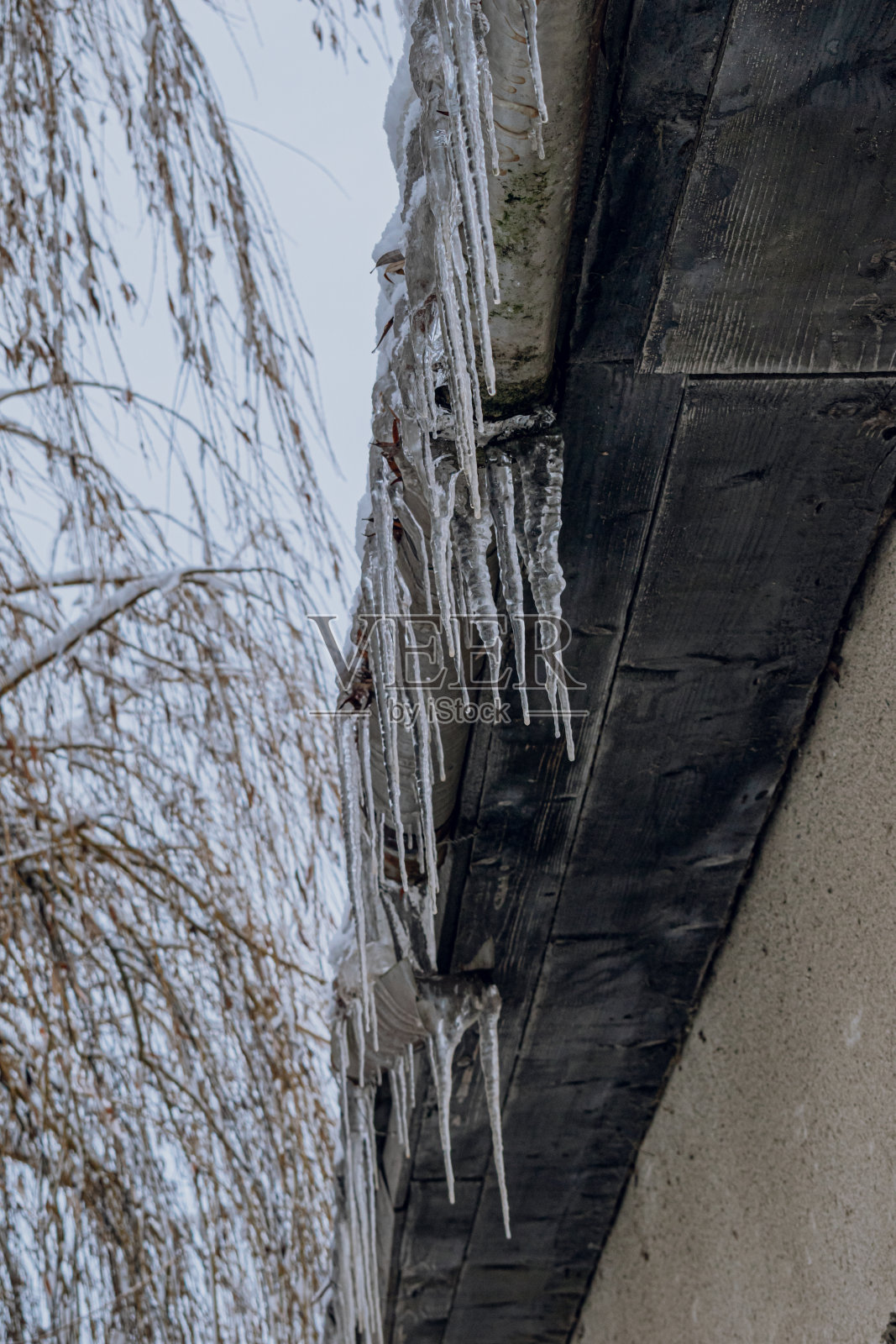 屋顶上的雪融化后形成的冰柱。照片摄影图片