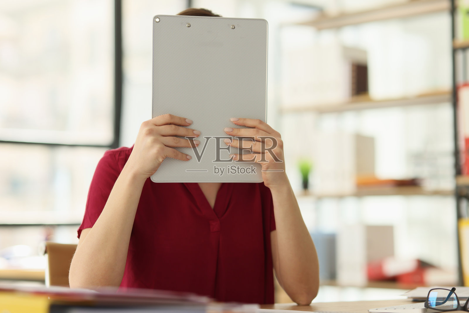 秘书坐在桌旁把脸藏在写字板后面照片摄影图片