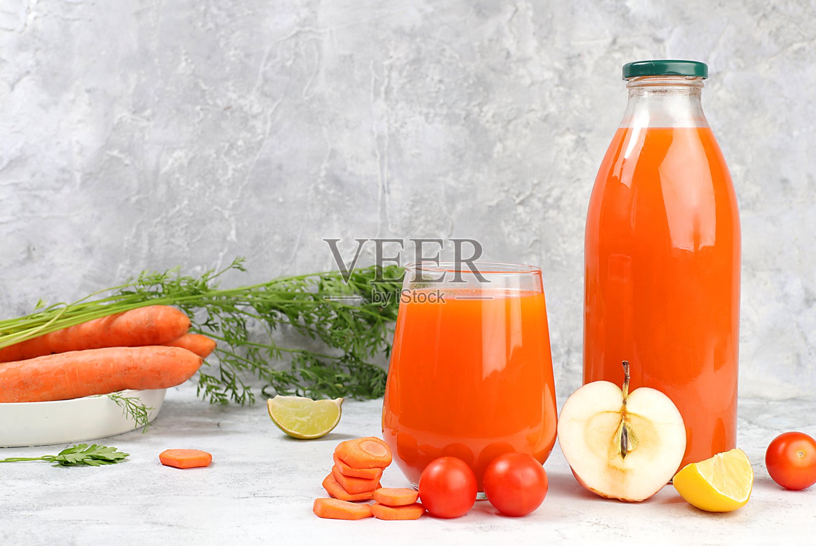 排毒饮料装在玻璃罐里和玻璃杯里，胡萝卜片、苹果片和西红柿片放在灰色的背景上。新鲜的天然胡萝卜苹果冰沙或果汁，减肥概念，新鲜水果和蔬菜照片摄影图片
