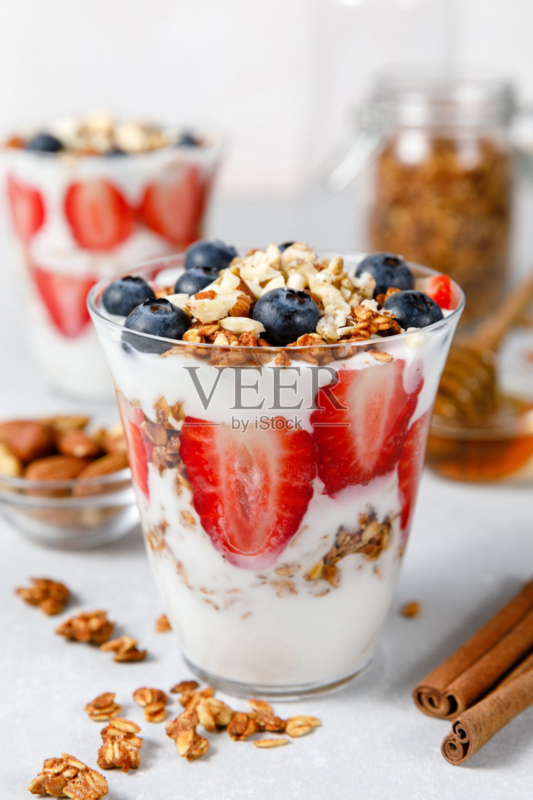 格兰诺拉燕麦糕配希腊酸奶、燕麦格兰诺拉燕麦卷、新鲜浆果、蜂蜜和薄荷叶，装在高玻璃罐中。健康的早餐概念。有机燕麦、杏仁和葵花籽照片摄影图片