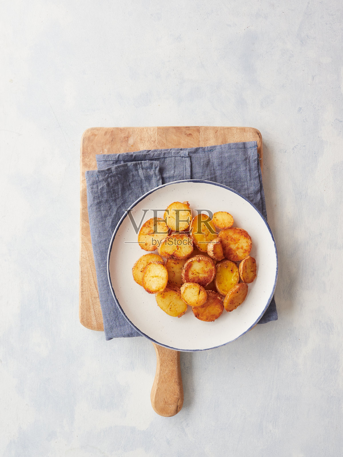 在蓝色的餐巾和木板上，盘子里放着脆皮金黄的烤土豆片。带复制空间的俯视图。照片摄影图片