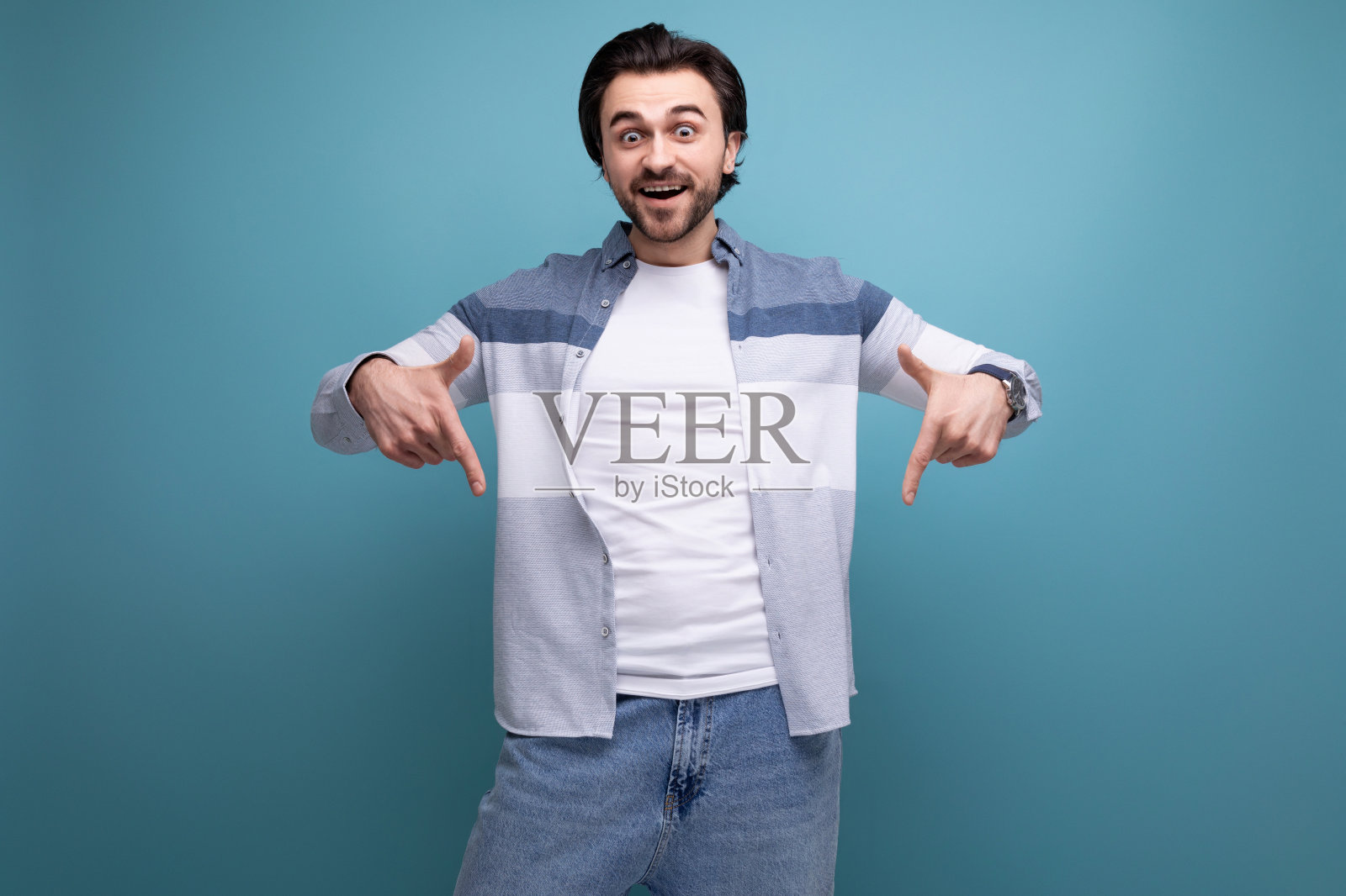 身穿毛衣、体格健壮的黑发青年雄心勃勃地指着摄影棚背景上的新闻照片摄影图片