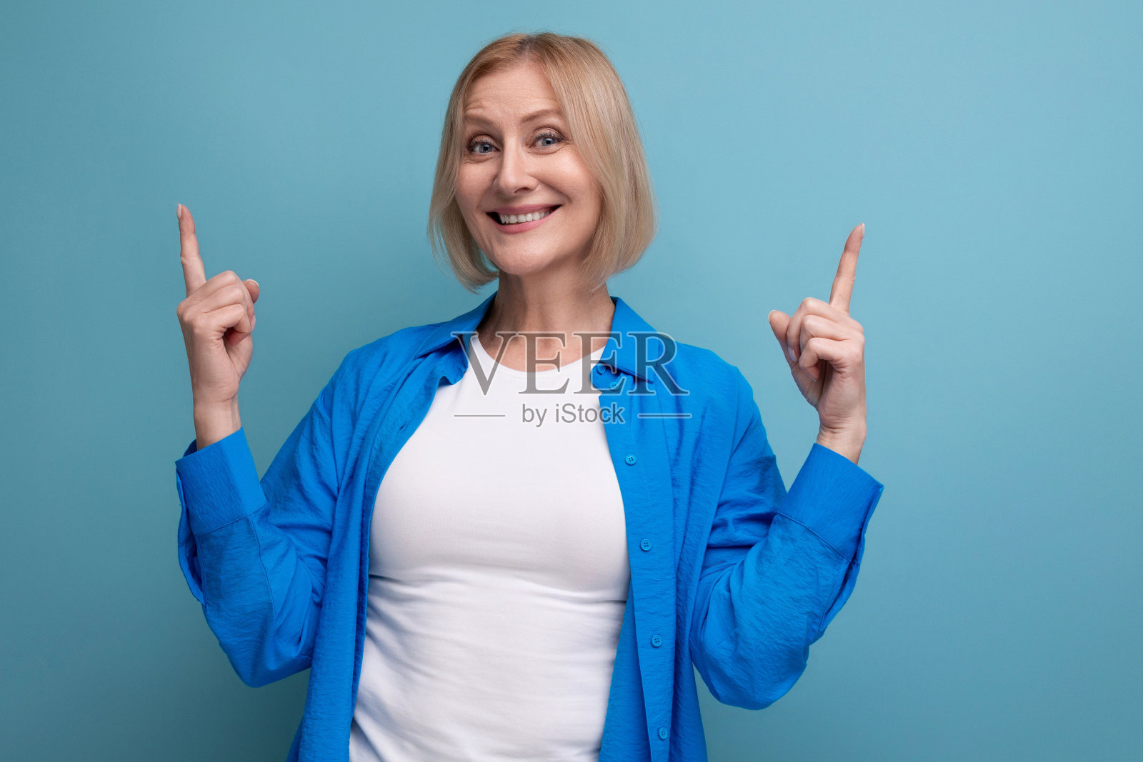 60年代开朗的金发女人的肖像，穿着休闲时尚的衬衫，双臂交叉在工作室背景上照片摄影图片