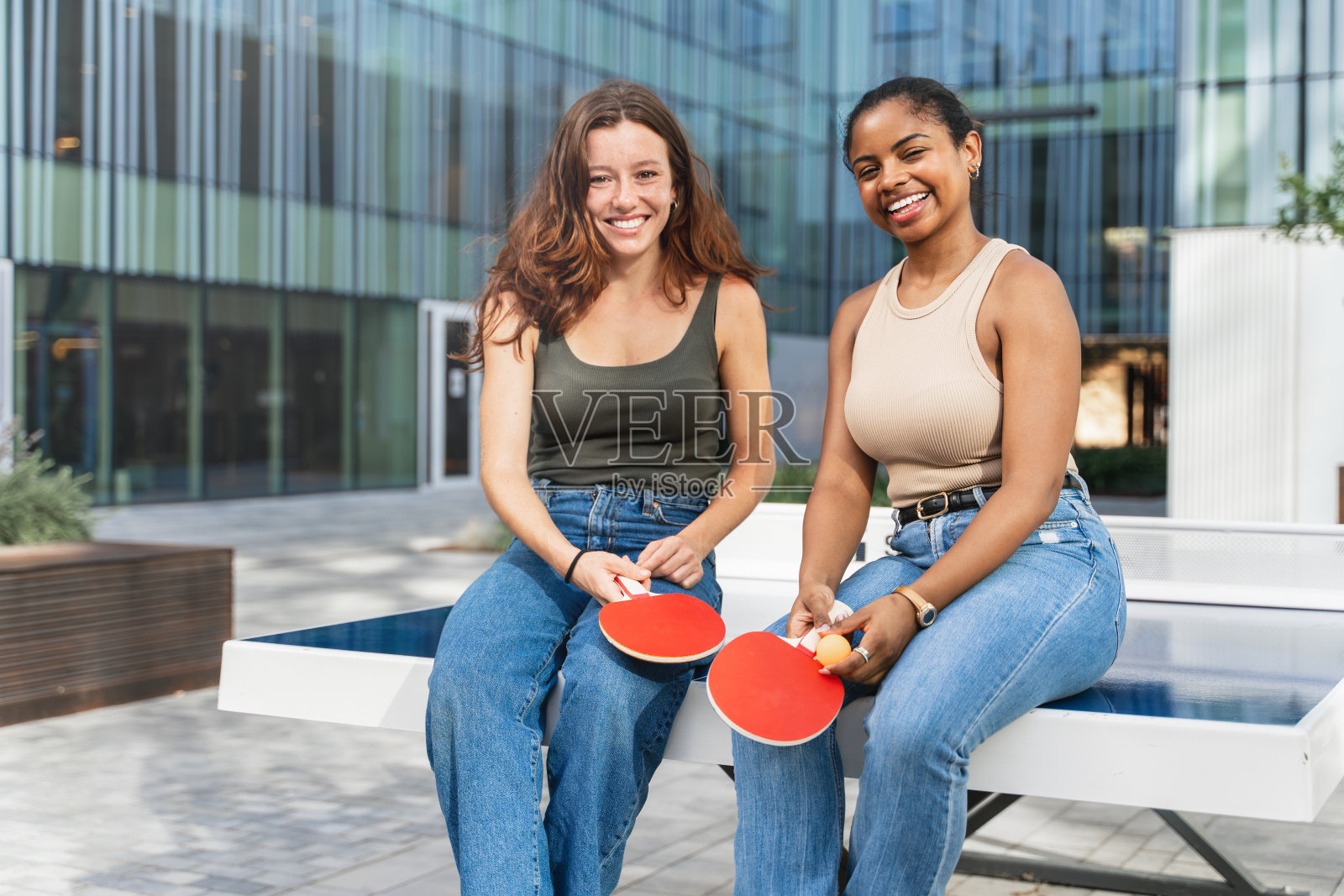 在大学校园里打完网球后，微笑的女孩们坐在乒乓球桌上照片摄影图片