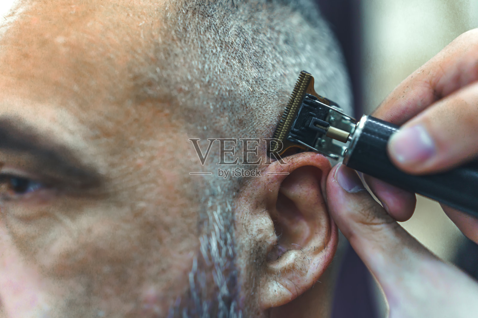 近距离专业理发师为男性客户用剪发器理发，在理发店为男性做美容。照片摄影图片