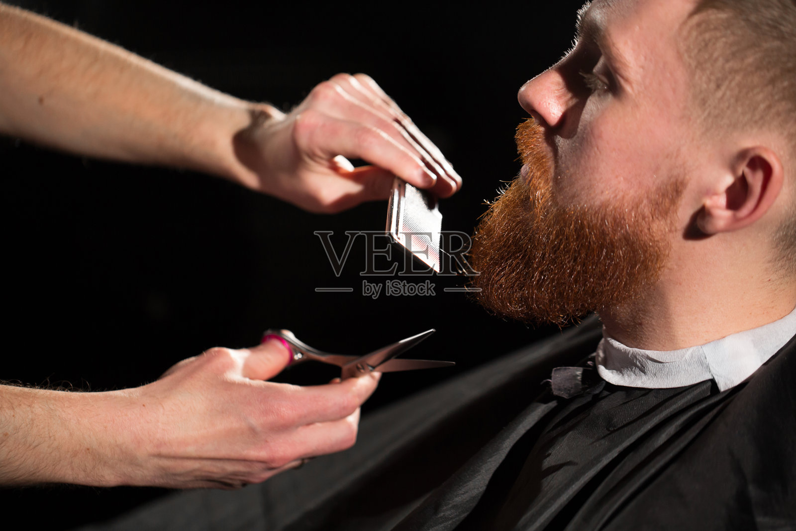 主人在理发店理发和刮胡子。理发师用剪刀和金属梳子做发型照片摄影图片